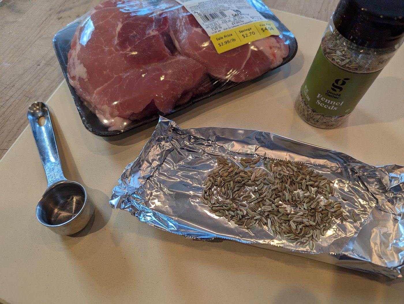Pork sirloin chops, a measuring cup, and fennel seeds laid out on a cutting board