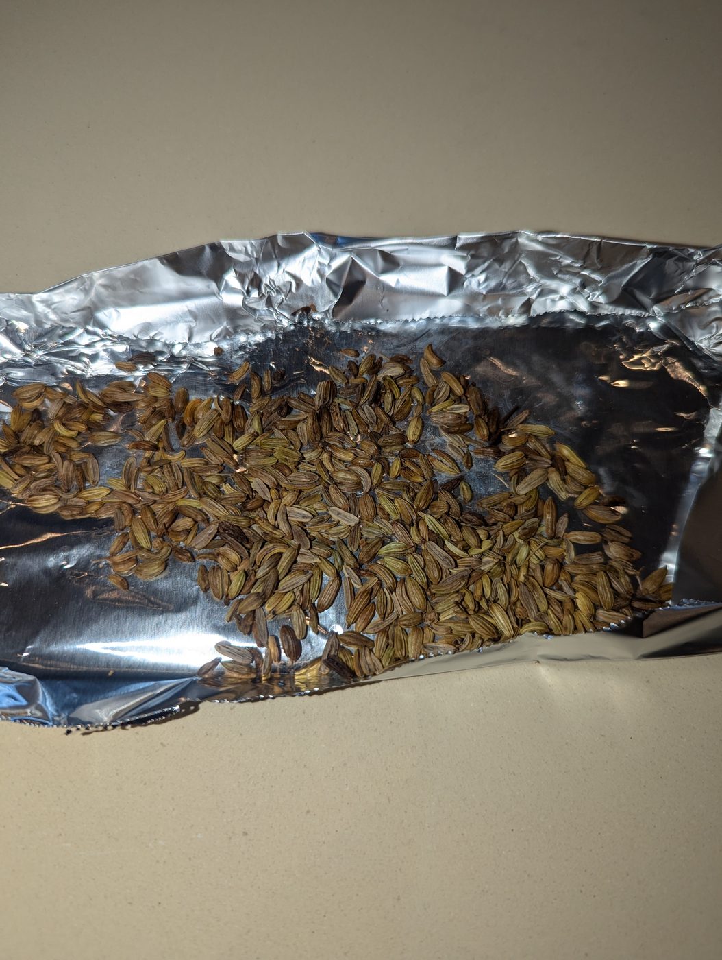 Toasted fennel seeds on a small aluminum foil tray